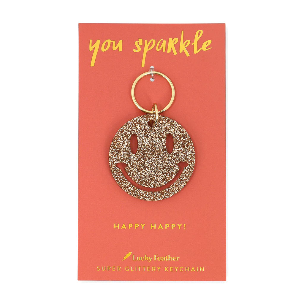 Gold glitter smiley face keychain on a 'you sparkle' card with Lucky Feather branding.