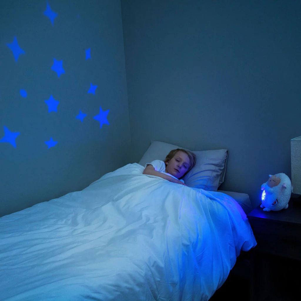 Lumieworld Lumipets Lamb Nursery Sound Soother with night light, white plush lamb on nightstand projecting blue stars in darkened bedroom.