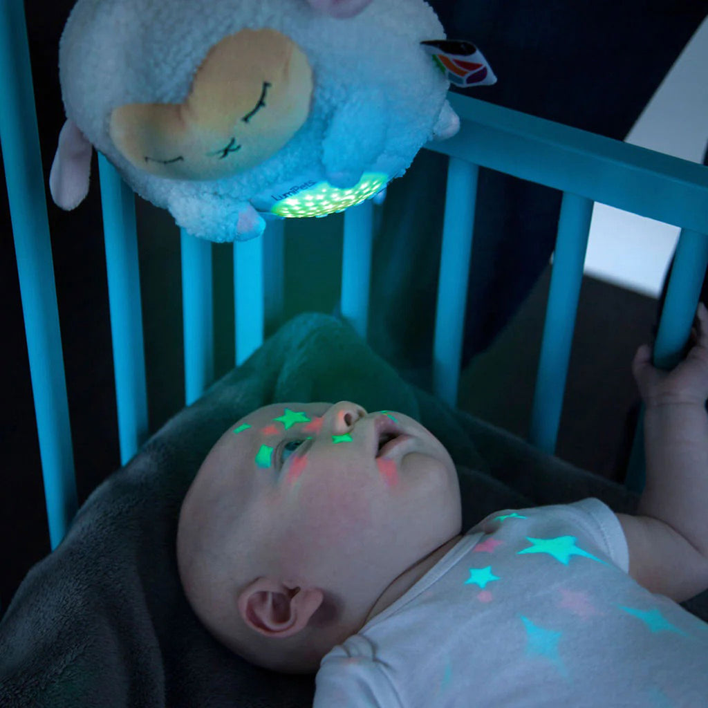 Lumieworld Lumipets Lamb Nursery Sound Soother with night light, white plush lamb fastened to the top of a crib with a baby looking at lights on its belly.