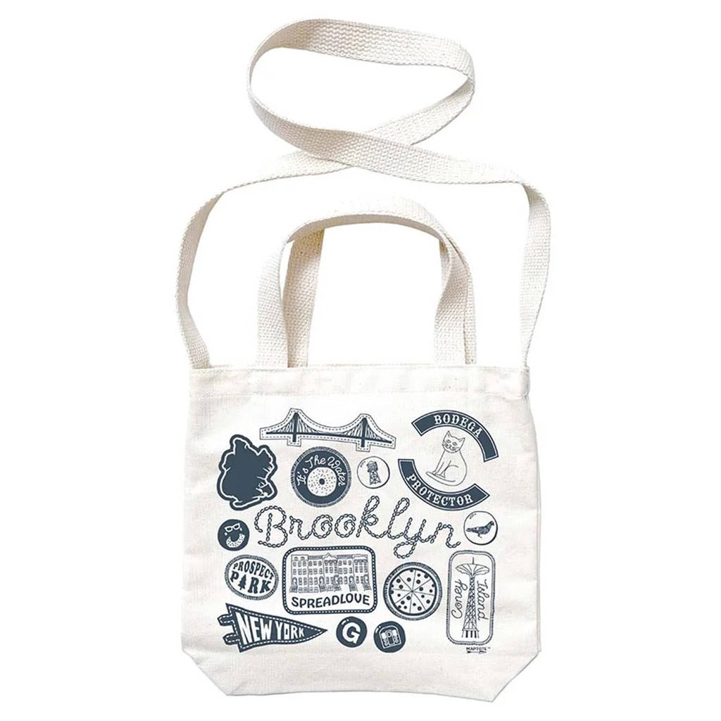 White tote bag with blue Brooklyn graphics and text, with white webbed handles and shoulder strap, on a white background.