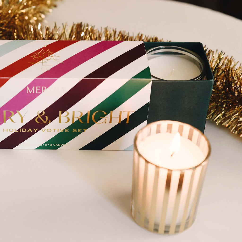 Mer-Sea Good Tidings gold striped holiday votive set with pink, red, green striped box packaging and "merry & bright" in gold foil lettering. Inner sleeve with votives is partially out.