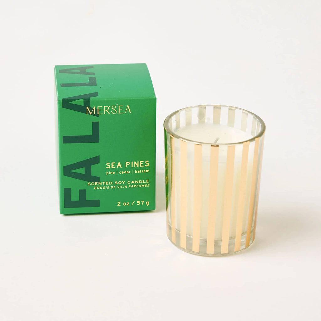 Mer-Sea Good Tidings Sea Pines scented votive candle in gold striped vessel, beside green box packaging.