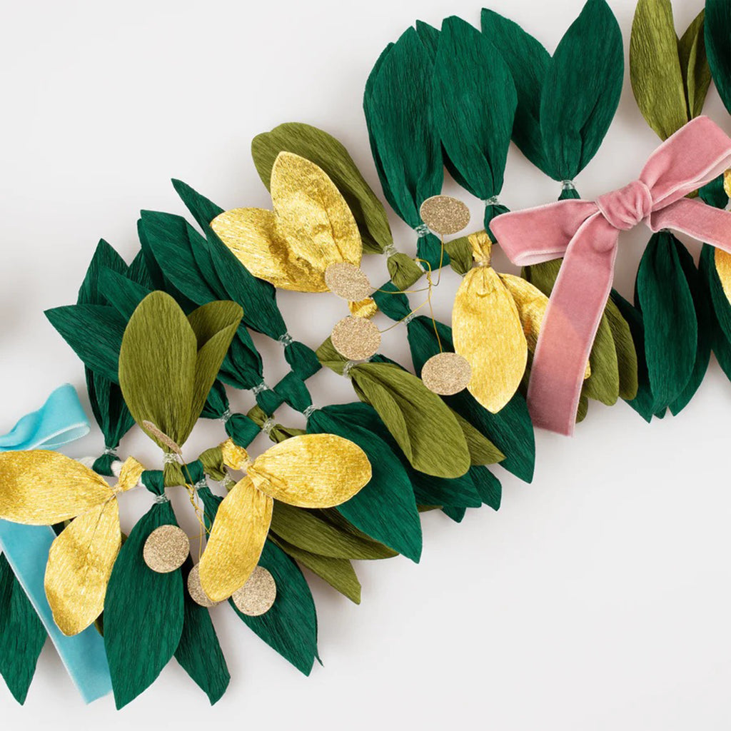 Meri Meri Paper Foliage Garland with crepe paper leaves in green and gold and velvet bows in rich red, dusty blue, dusty pink and mustard, detail.