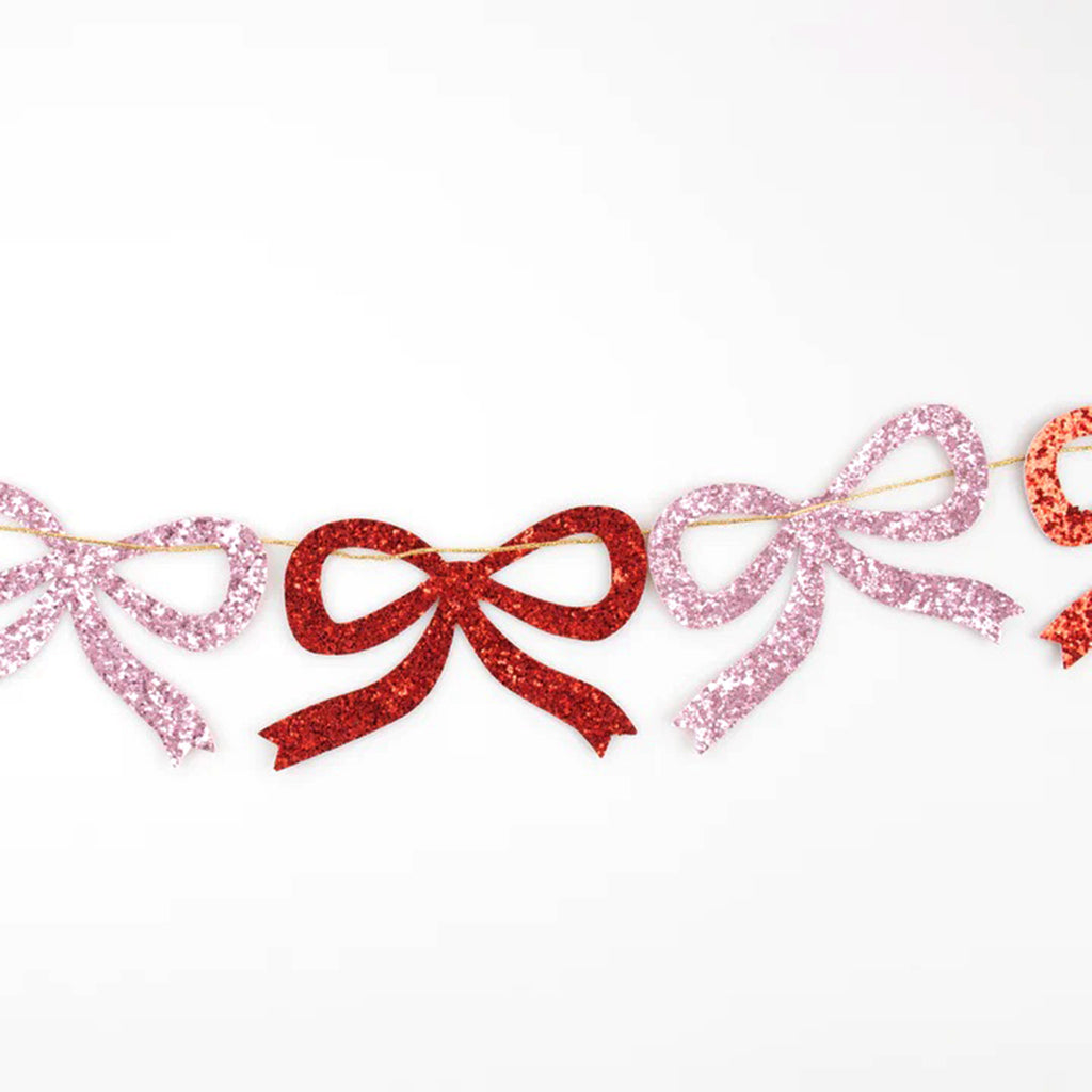 Meri Meri Red & Pink paper glitter bow garland holiday party decoration, detail of bows strung on gold metallic thread. 