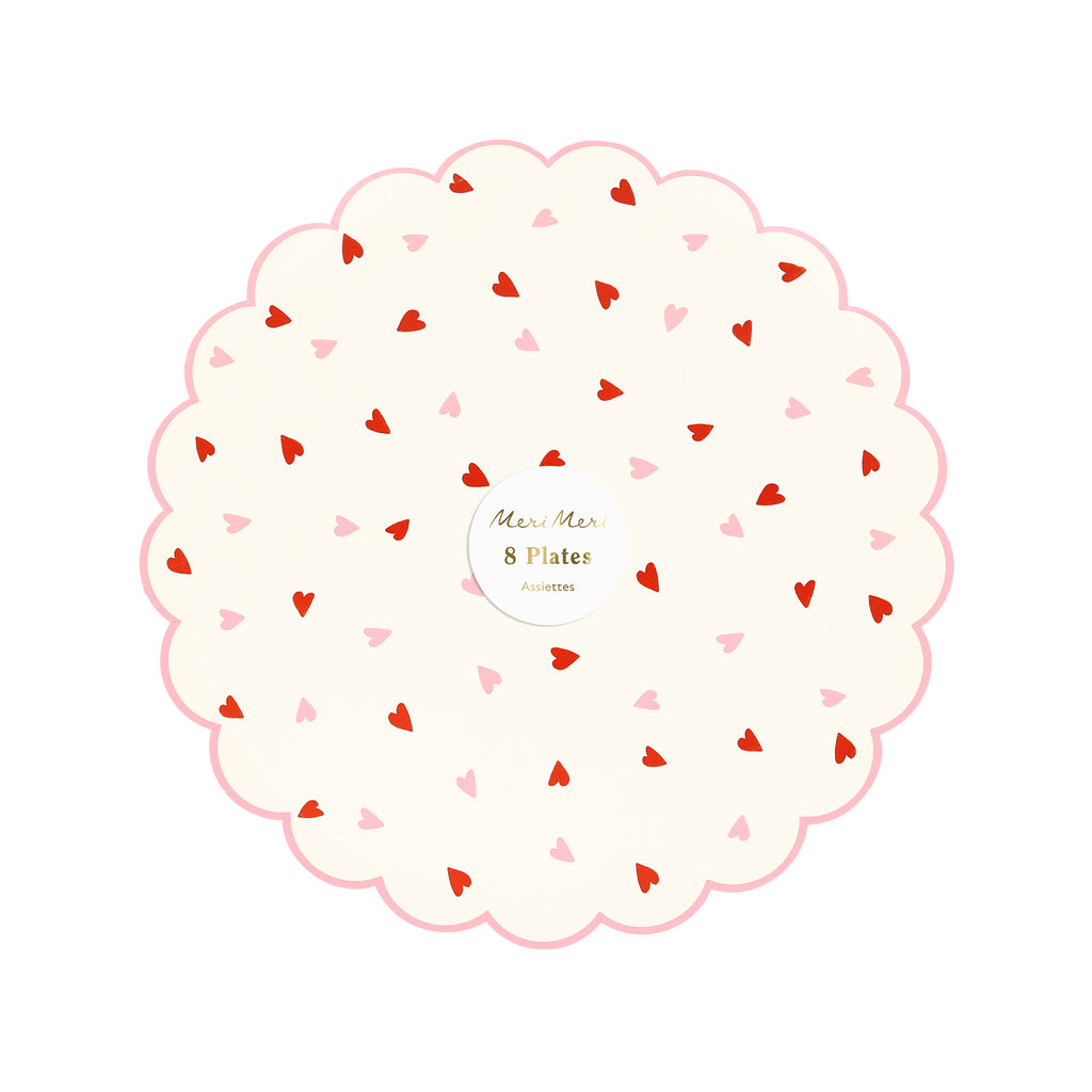 Meri Meri Valentine's Day party paper plates with small red and pink hearts on a white backdrop and a scalloped edge with pink trim, in packaging.