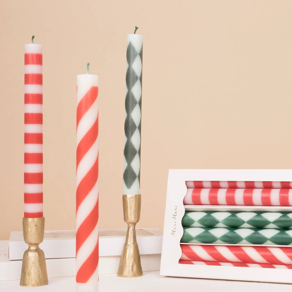 Meri Meri Festive Stripe unscented red and green patterned unscented candles in box packaging, with some beside in a gold taper holder.