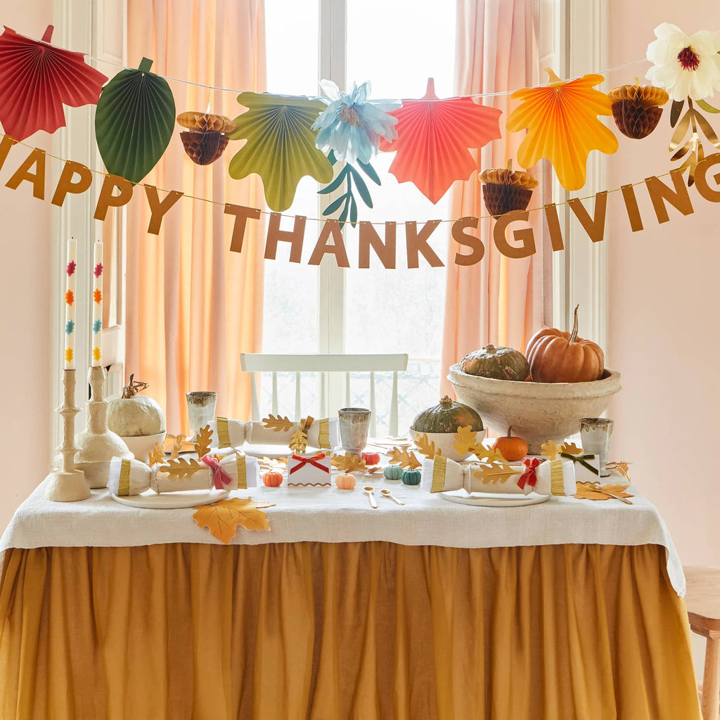 Meri Meri Happy Thanksgiving garland with honeycomb acorns, fan leaves and flowers, both strands shown full length above a thanksgiving table.