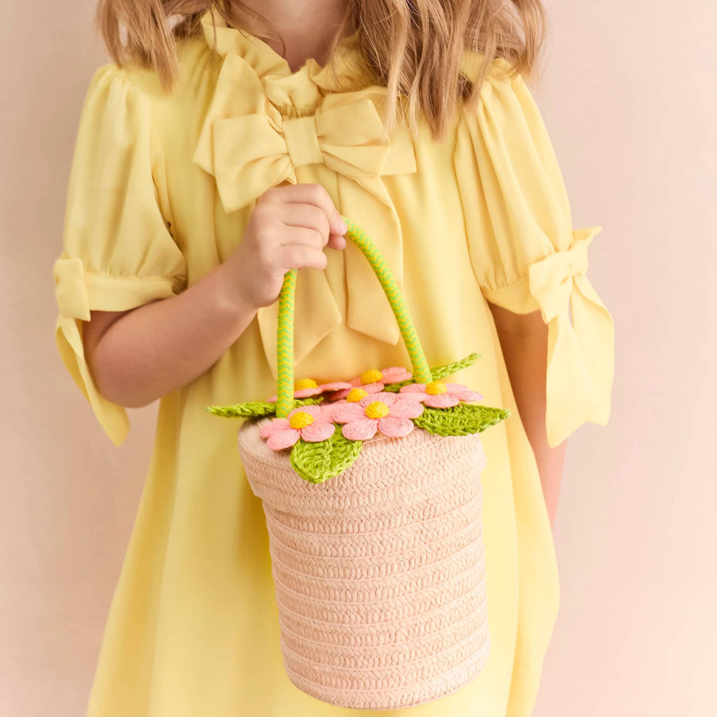 Meri Meri Flower Pot woven paper basket bag with handle, being held by a child in a yellow dress.