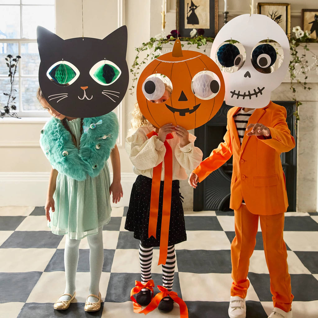 Three children wearing Halloween-themed masks and costumes in a room with a checkered floor.