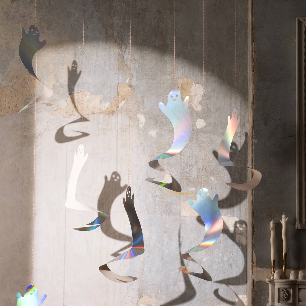 Iridescent spinning ghost paper figures with a light shining on them, hanging in a room with Halloween decor.
