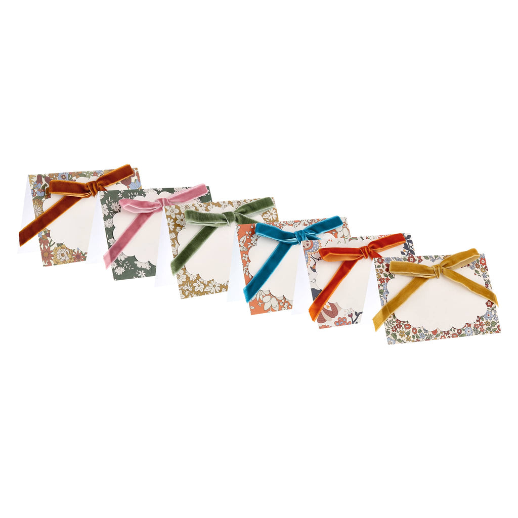 Set of six place cards with floral print and velvet bows, on a white background.