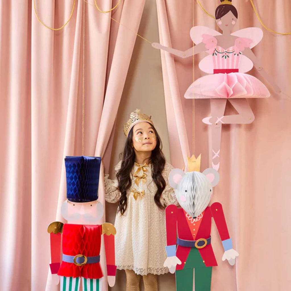 Child standing behind decorative Nutcracker and Mouse King figures with a ballerina figure on a pink curtain background.