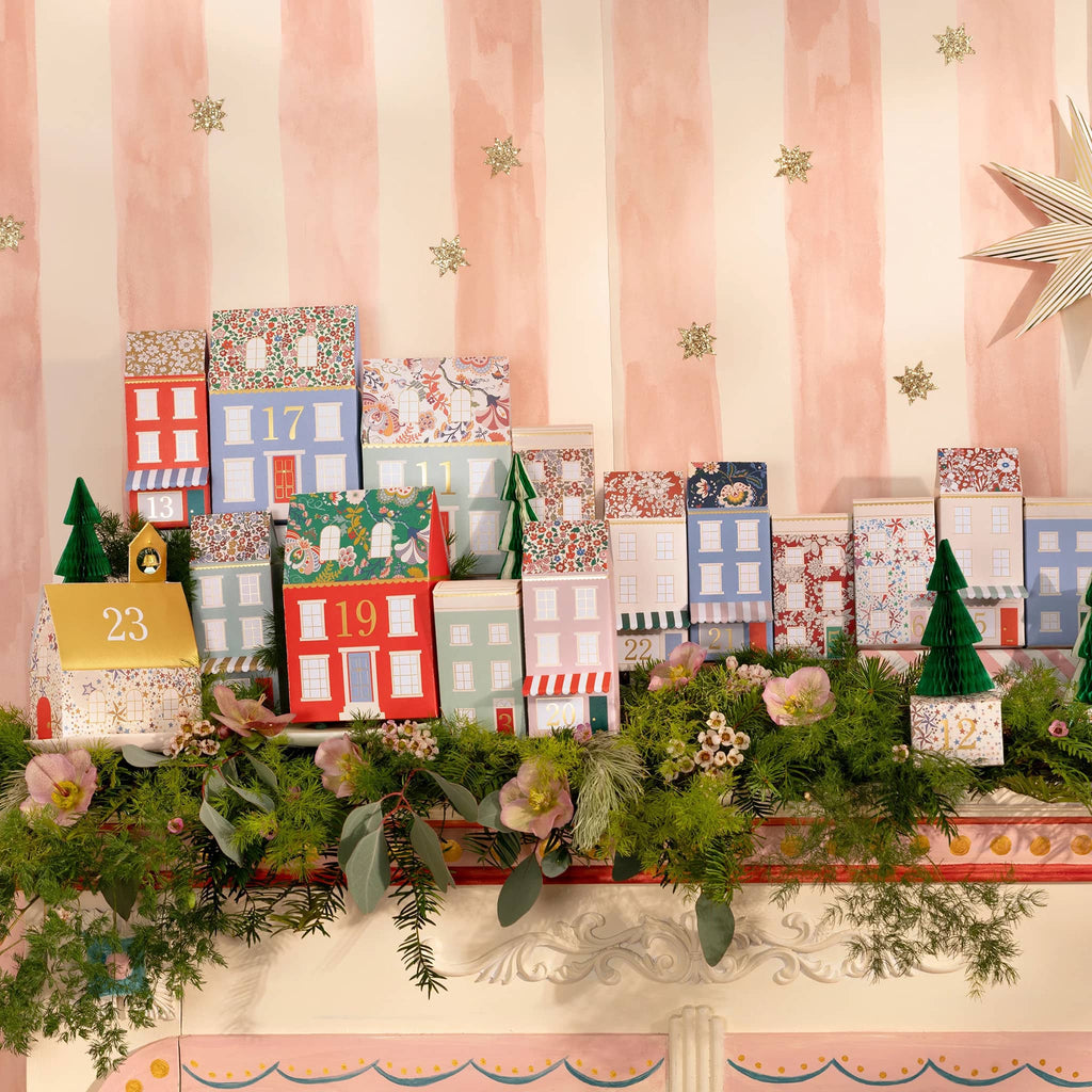 Set of Christmas-themed advent calendar box shaped houses with floral prints and numbers and honeycomb trees on a pink striped backdrop with garland.