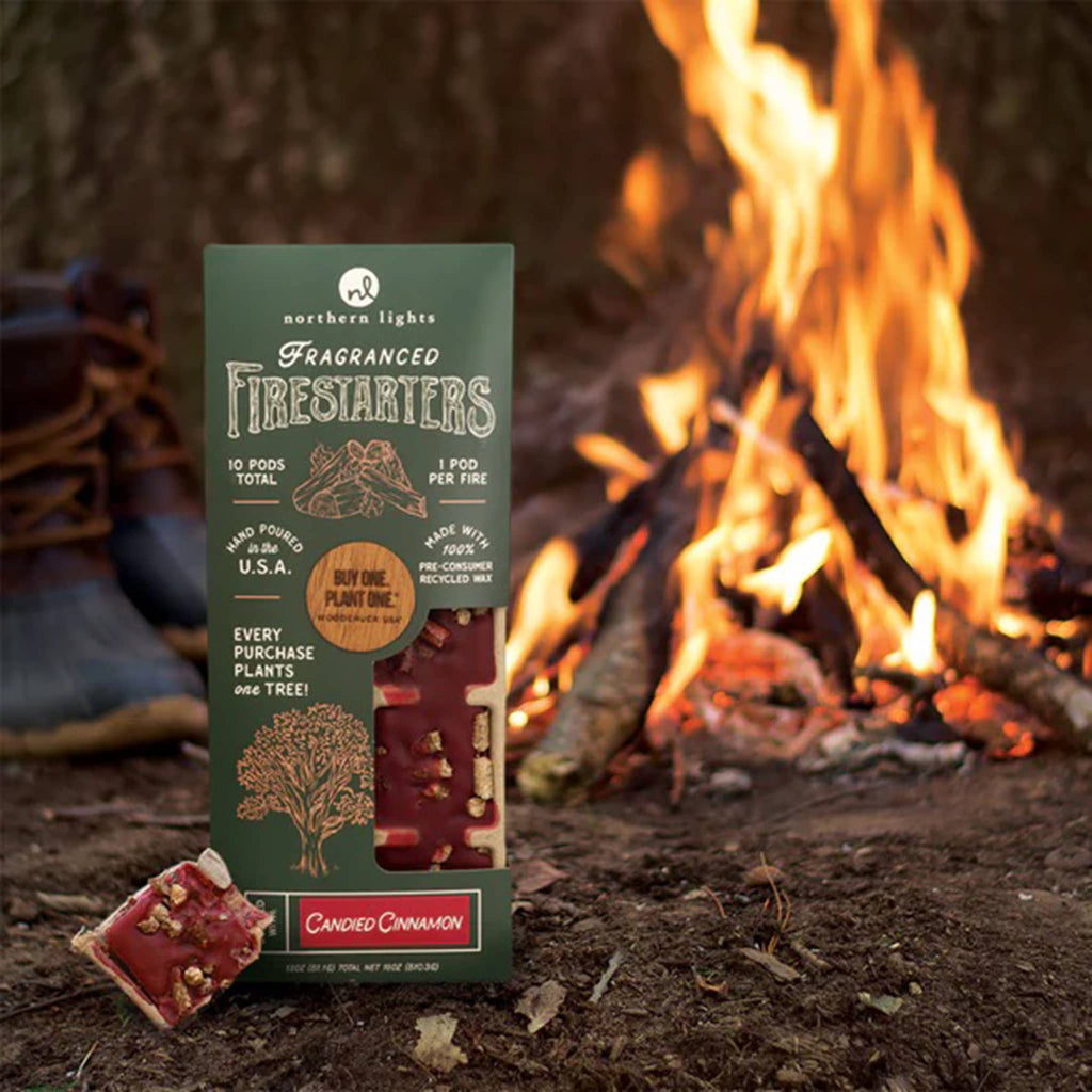 Northern Lights Fragranced Firestarters Candied Cinnamon scented wax pods in forest green packaging, in front of a campfire.