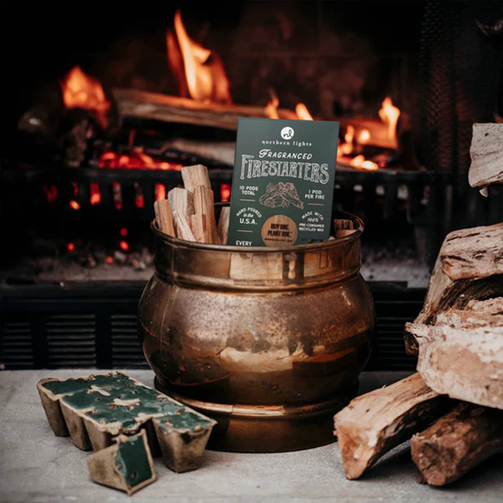 Northern Lights Fragranced Firestarters Evergreen Forest scented wax pods in forest green packaging, in front of fireplace.