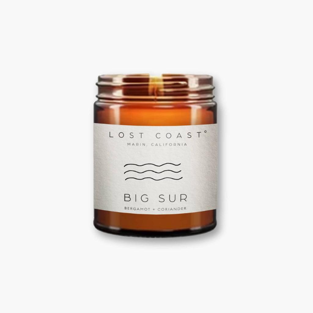 Lost Coast Big Sur bergamot and coriander scented soy wax blend candle in amber jar, lid off and wick lit, on white background.