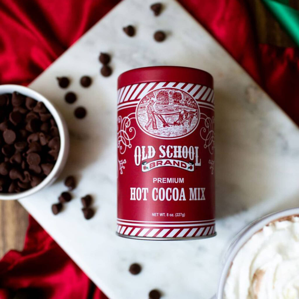 Old School Brand hot cocoa mix in red and white tin canister on a marble background with chocolate chips.