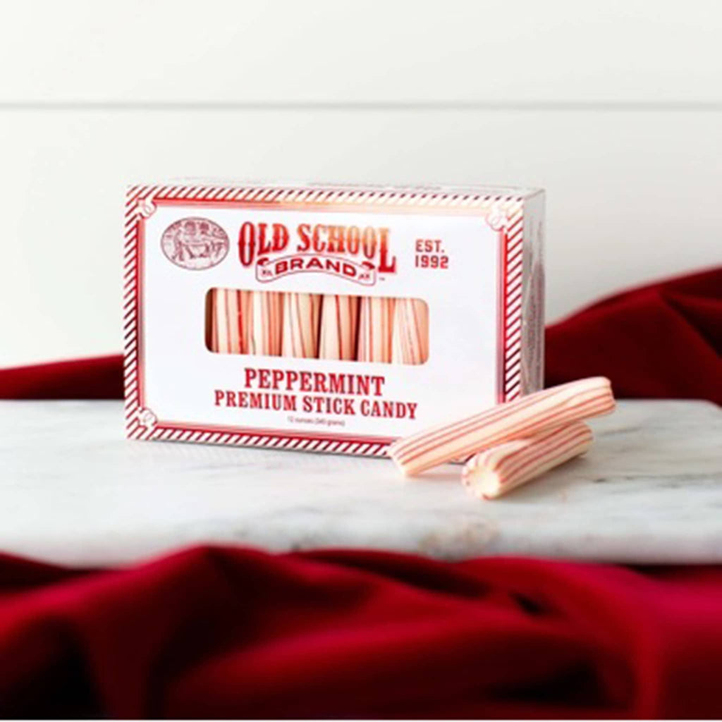 Peppermint stick candy beside a red and white striped box with Old School Brand, on a marble surface with red tablecloth.