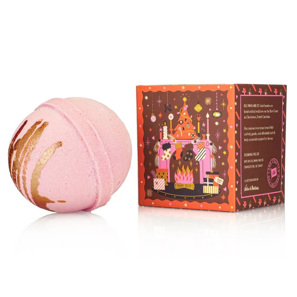 Pink bath bomb with gold drizzle next to its decorative box on a white background.