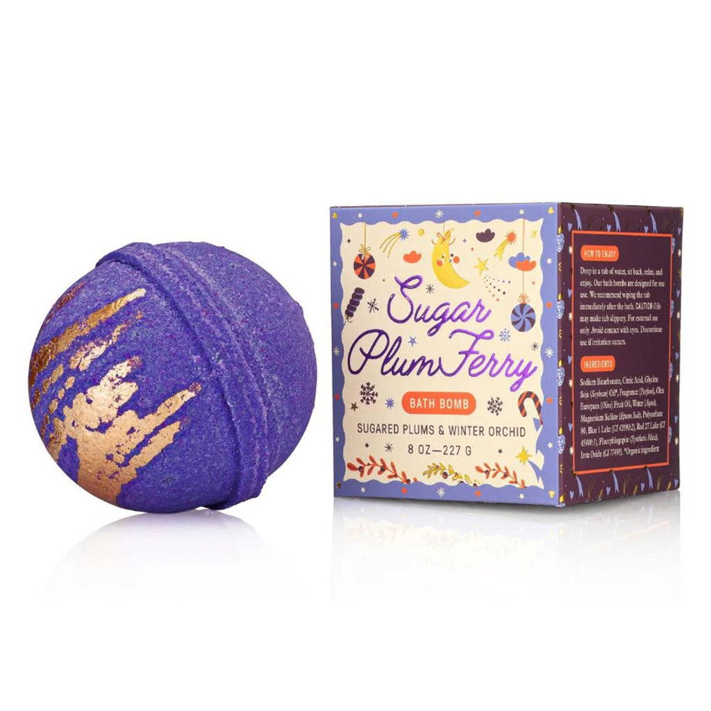 Purple bath bomb with gold accents next to its packaging on a white background.