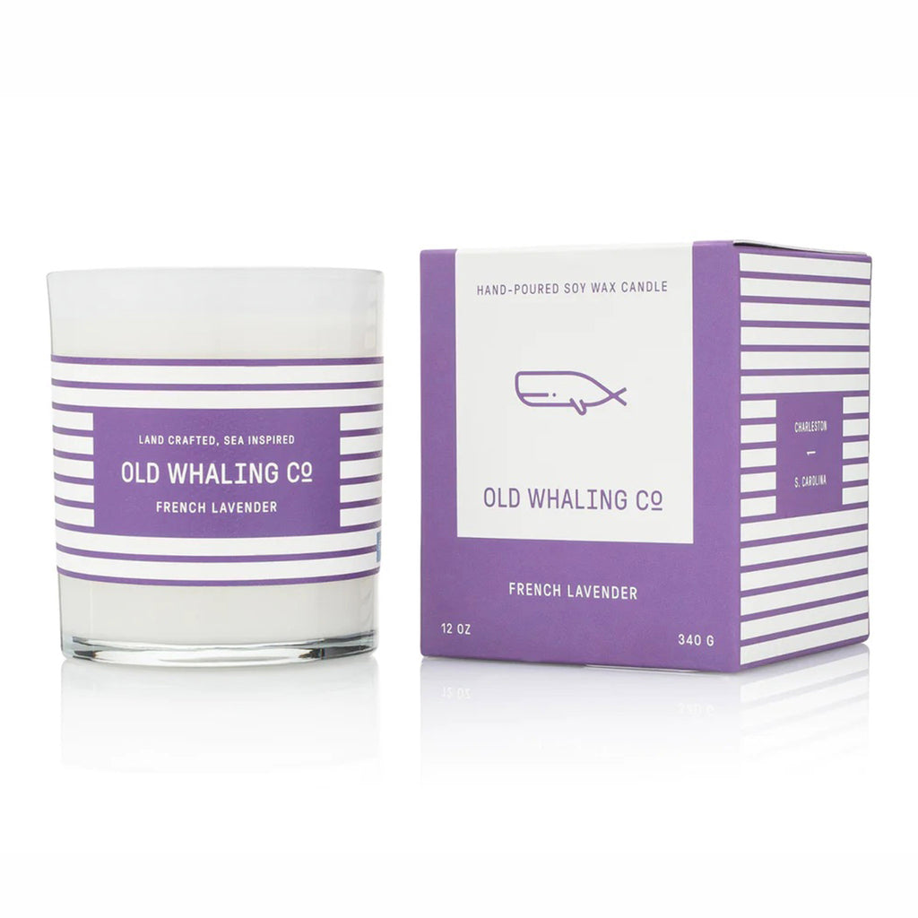 Old Whaling Company French Lavender 12 ounce scented olive oil and soy wax blend candle in an opaque white glass vessel with purple and white striped label beside matching purple gift box.