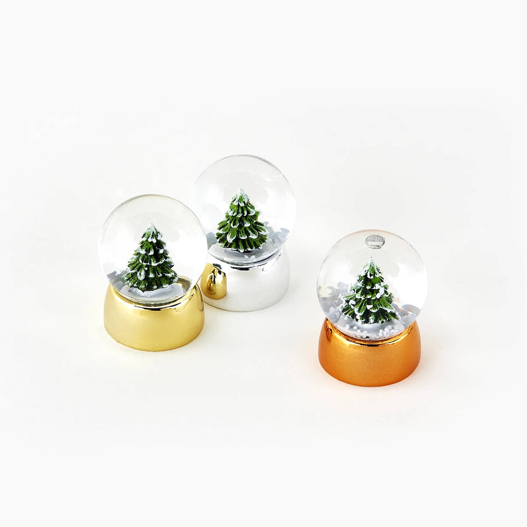 Three small snow globes with snowy trees  inside on gold, silver, and bronze bases, on a white background.