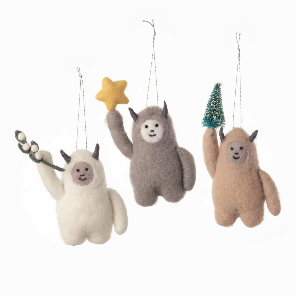 Set of three plush abominable snowman yeti ornaments in different colors with props on a white background.