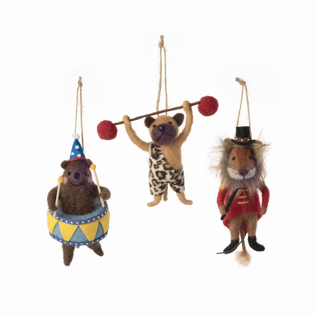 Three felt ornaments of animals in circus costumes hanging on strings against a white background.