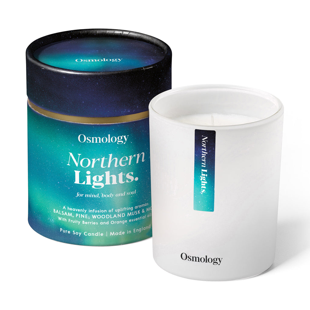 Osmology by Aery Living Northern Lights scented soy wax candle in matte white vessel with blue paper canister packaging with an illustration that looks like the northern lights in a night sky.