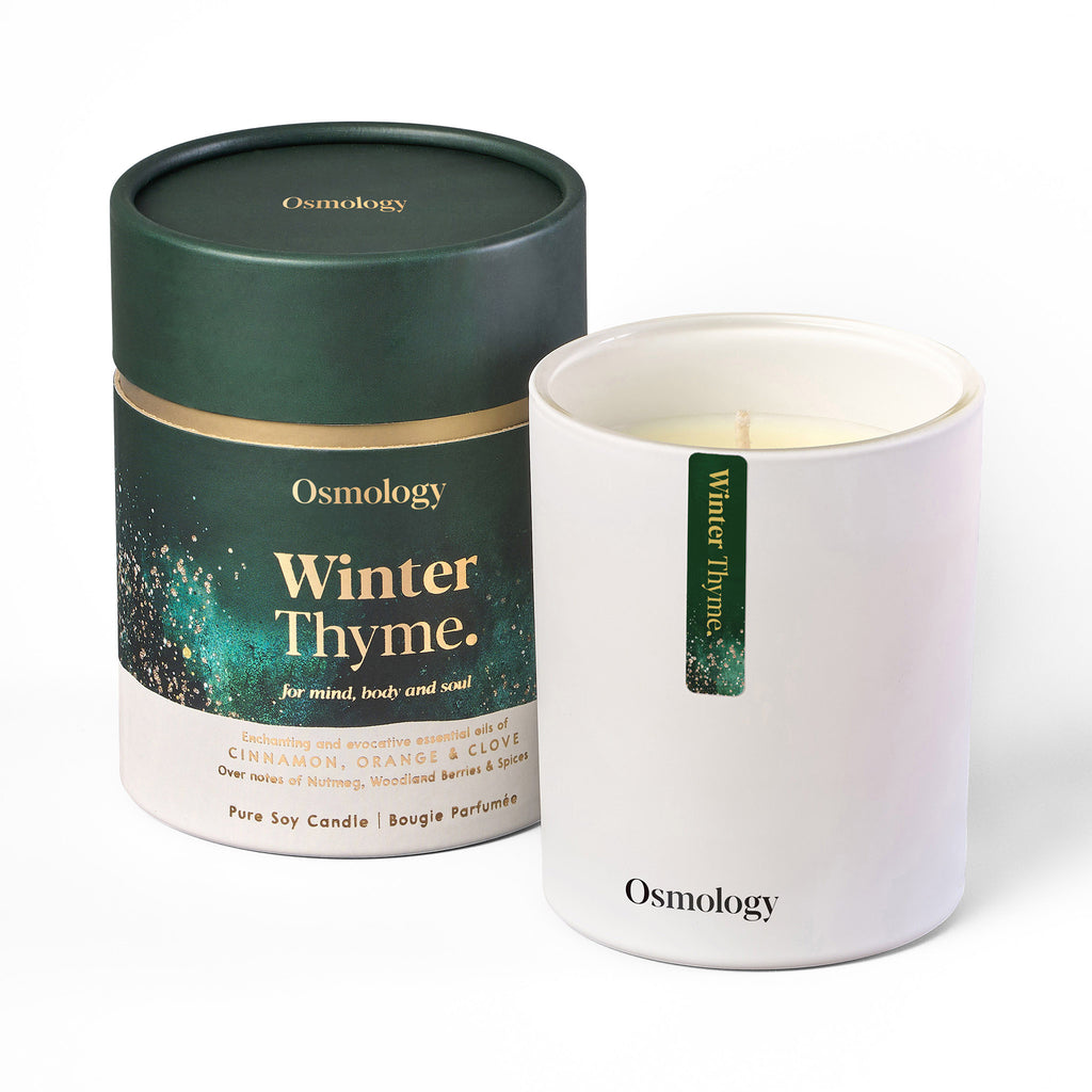 Osmology by Aery Living Winter Thyme scented soy wax candle in matte white vessel with dark green paper canister packaging with gold foil details.