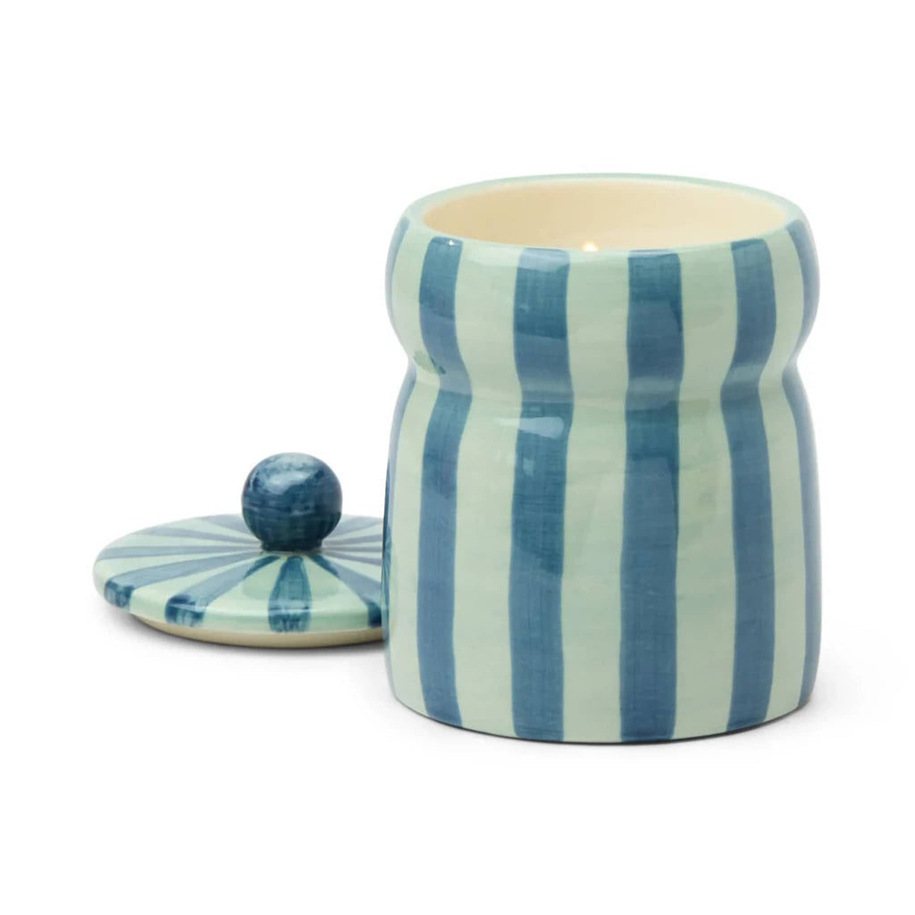 Warm Cider candle in ceramic jar with blue and teal stripes, lid off and wick lit, on a white background.