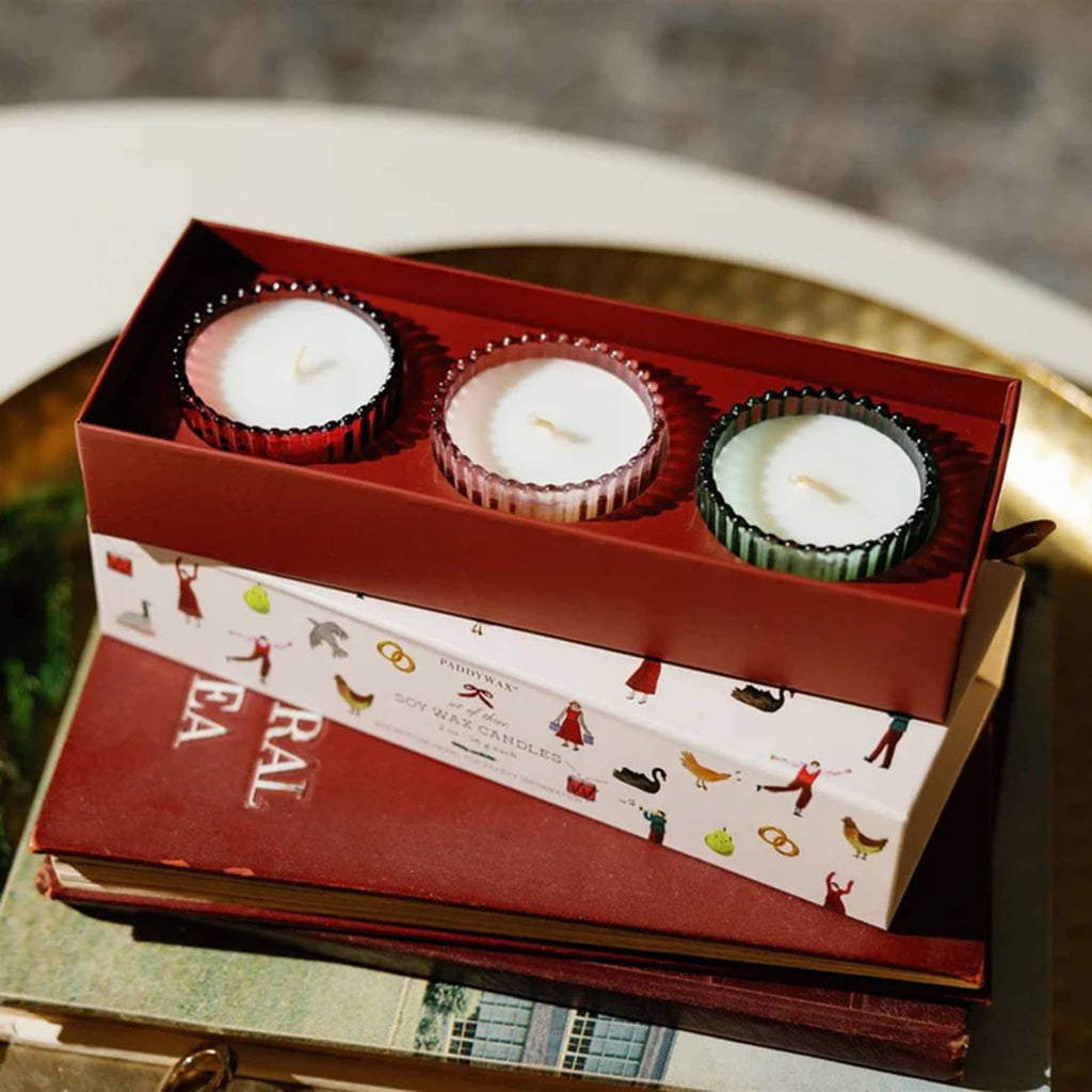 3 candles in holiday illustrated box on a stack of books.