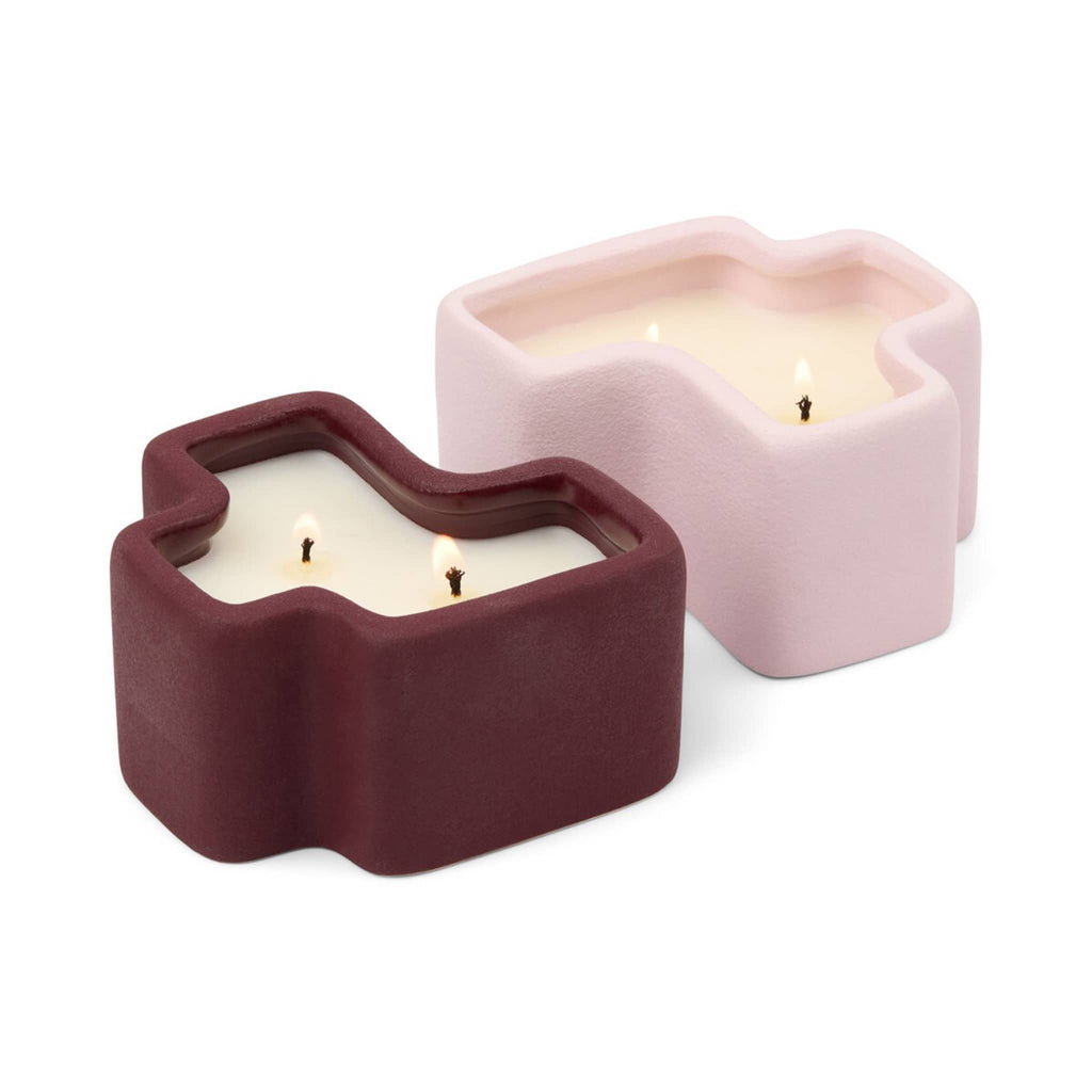 Two candle holders, one burgundy and one pink, with double wicks lit, on a white background.