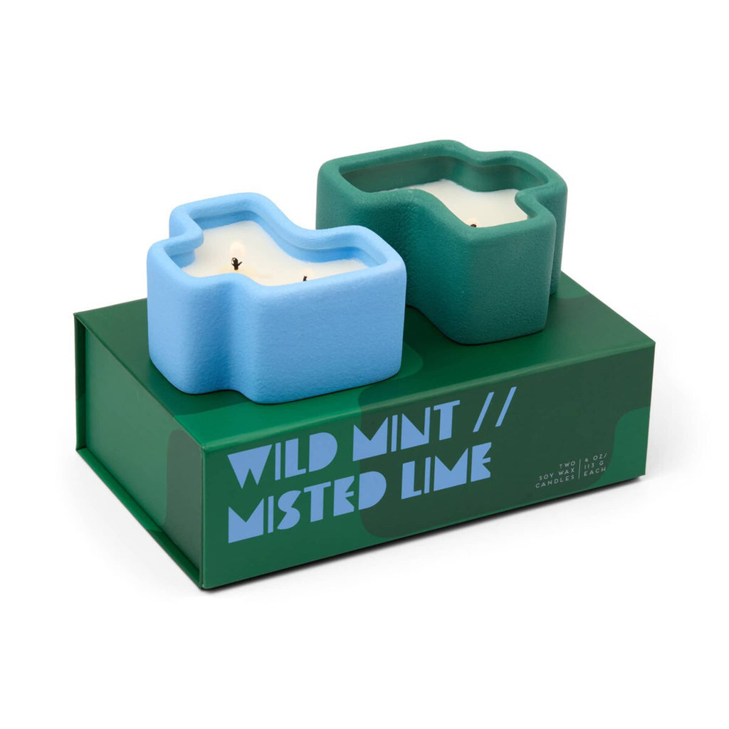Two ceramic candle holders in blue and green shaped like puzzle pieces with green box packaging with "Wild Mint and Misted Lime" text on a white background.
