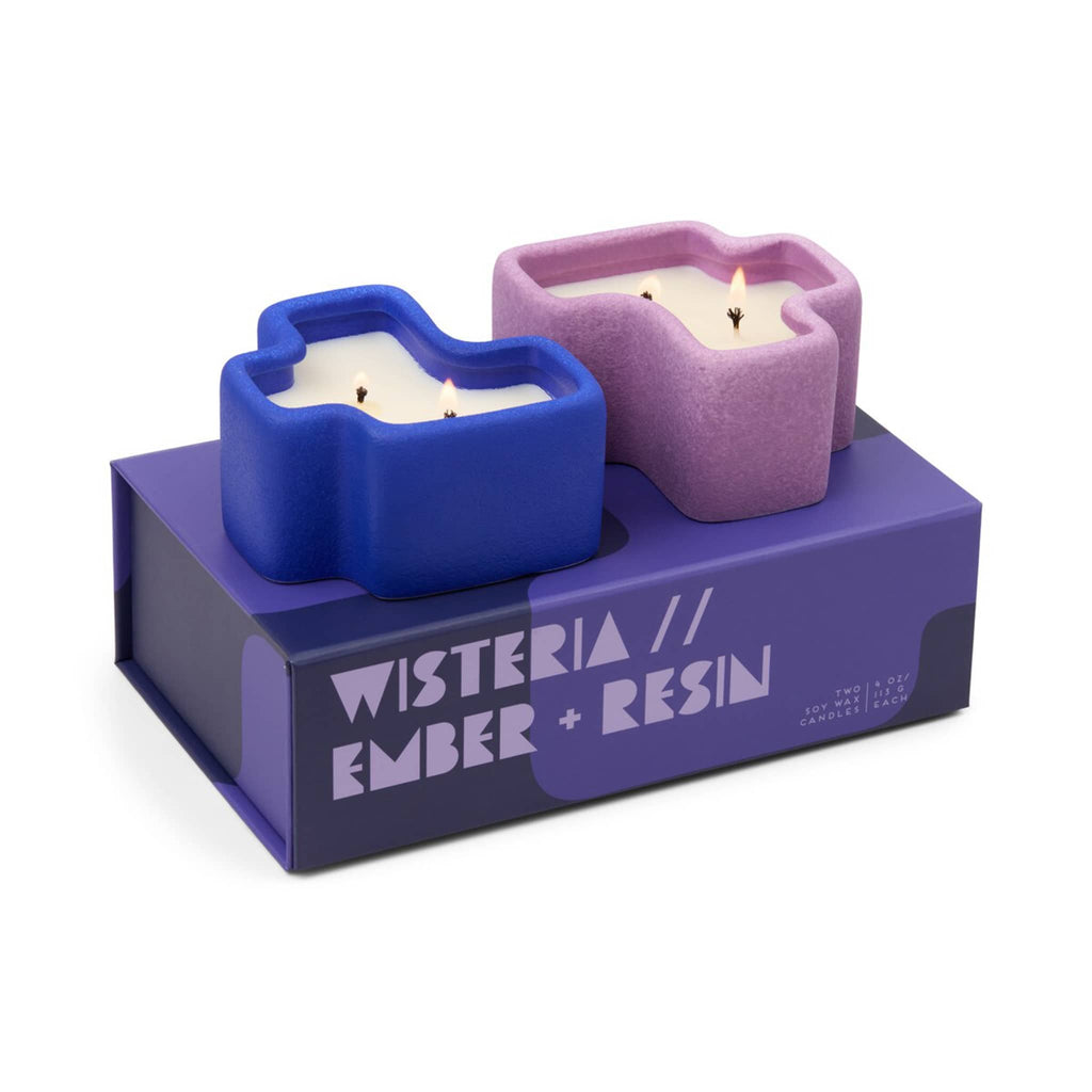 Two ceramic candle holders in cobalt blue and lilac, shaped like puzzle pieces with purple packaging with "Wisteria and Ember + Resin" text on a white background.