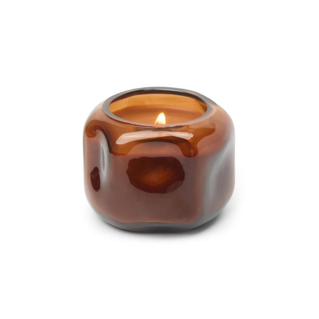 Amber glass organic shaped vessel with amber wax and lit wick, on a white background.