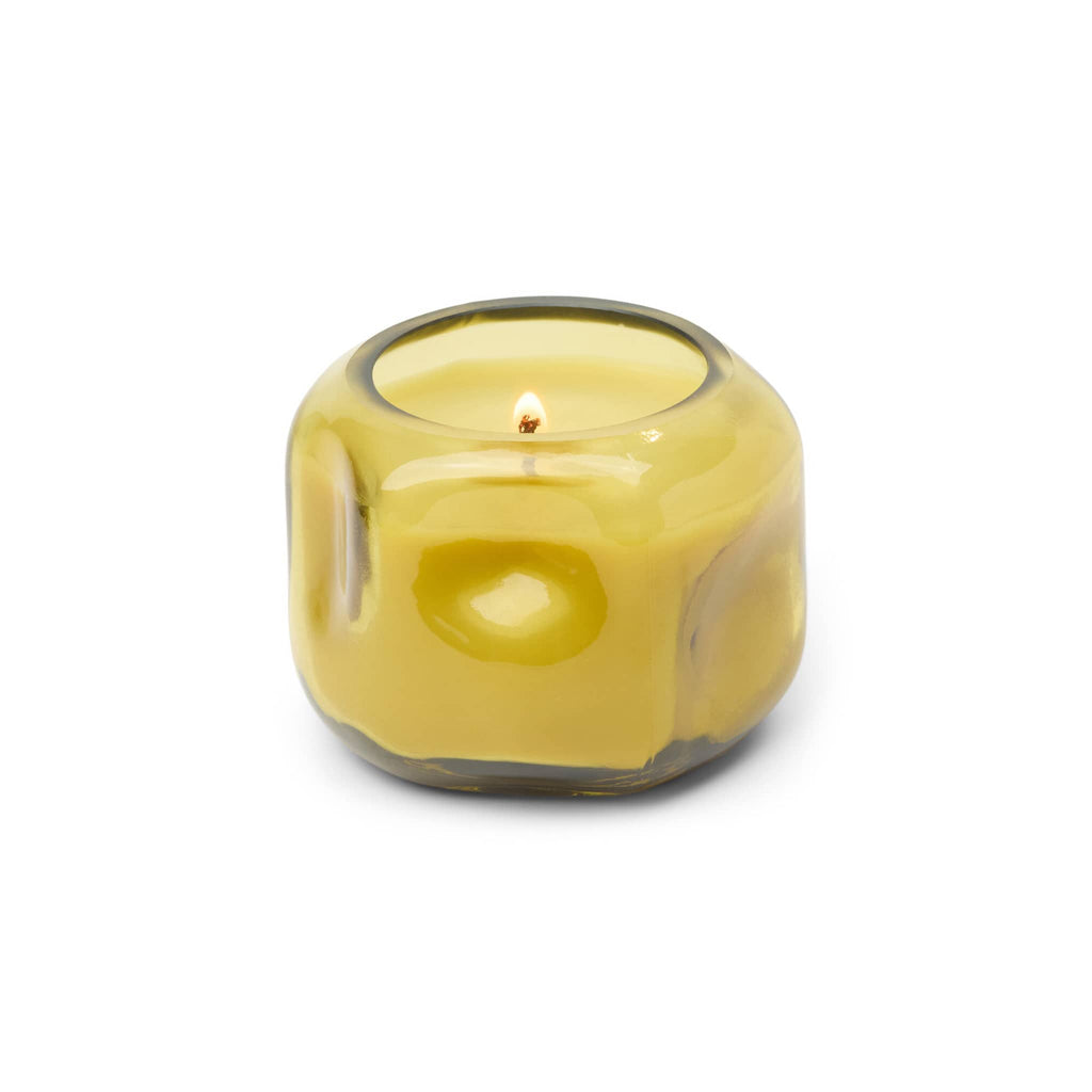 Yellow glass organic shaped vessel with yellow wax and lit wick, on a white background.