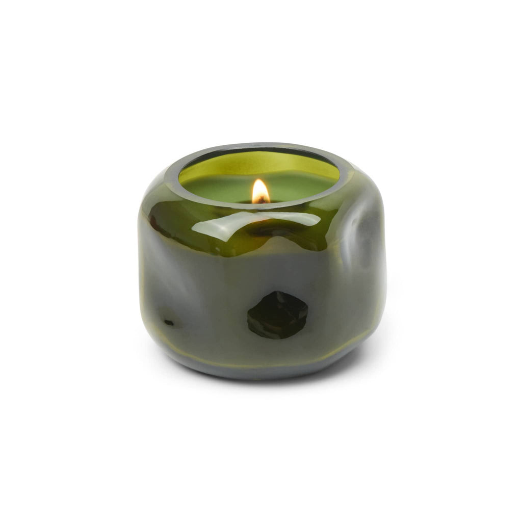 Green glass organic shaped vessel with green wax and lit wick, on a white background.