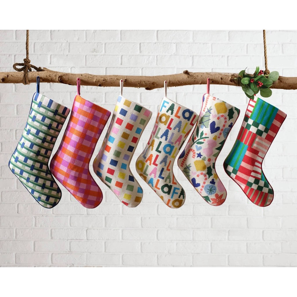 Colorful patterned stockings hanging on a branch against a white brick wall.