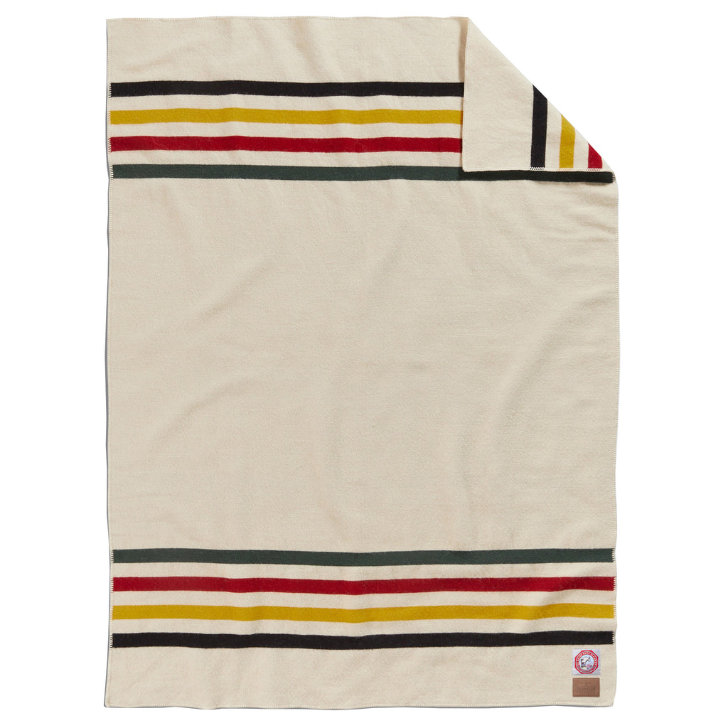 Pendleton Glacier National Park Throw Blanket in ivory with navy, yellow, red and green stripes at both ends, full blanket shown with a corner folded back.