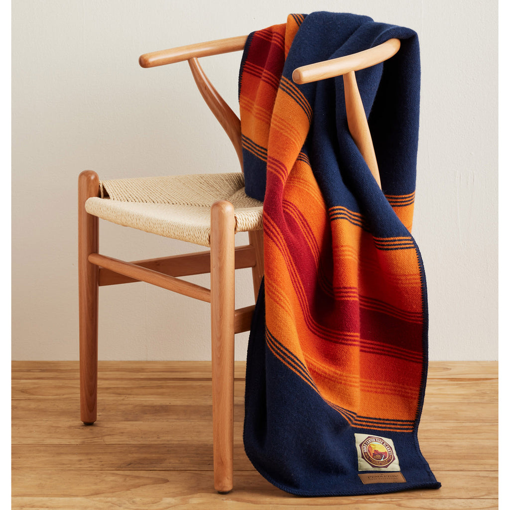 Pendleton Grand Canyon National Park Throw Blanket in navy with orange and red stripes at both ends, full blanket shown draped over a chair.