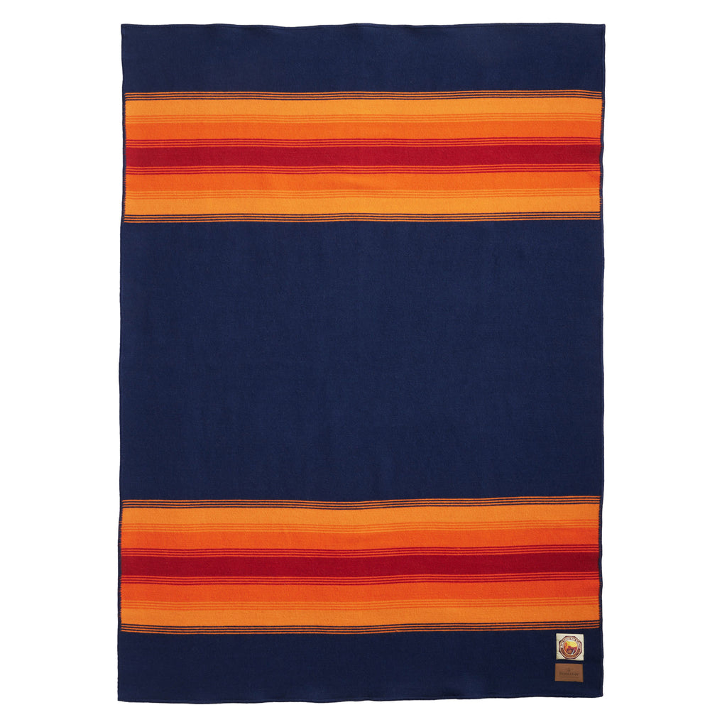 Pendleton Grand Canyon National Park Throw Blanket in navy with orange and red stripes at both ends, full blanket shown with a corner folded back.