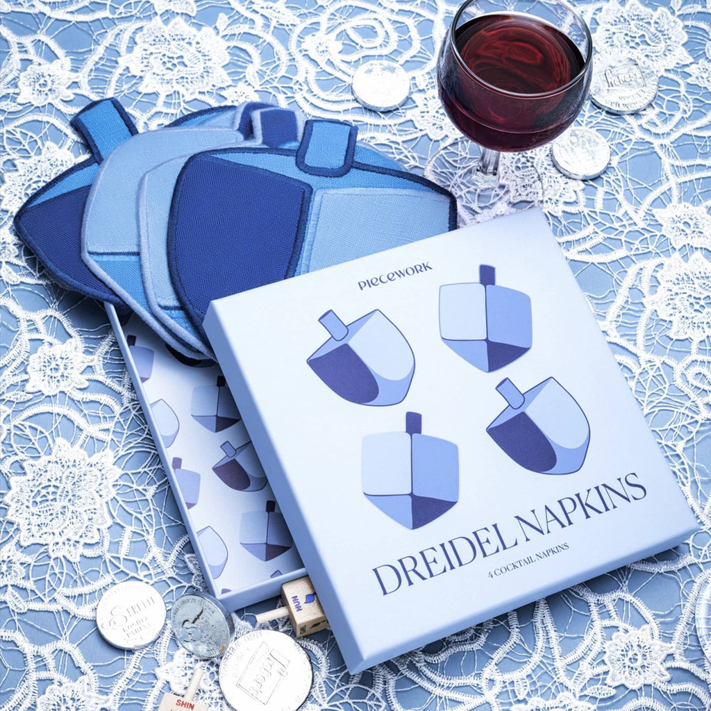 Set of dreidel napkins with a glass of red wine on a lace tablecloth.