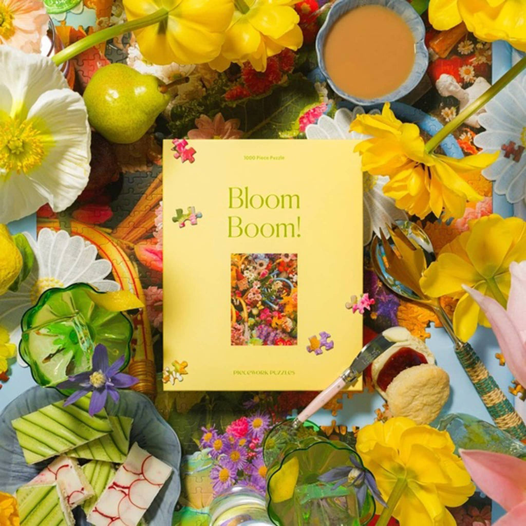 Piecework Puzzles 1000 piece Bloom Bloom! jigsaw puzzle in box packaging, surrounded by flowers.