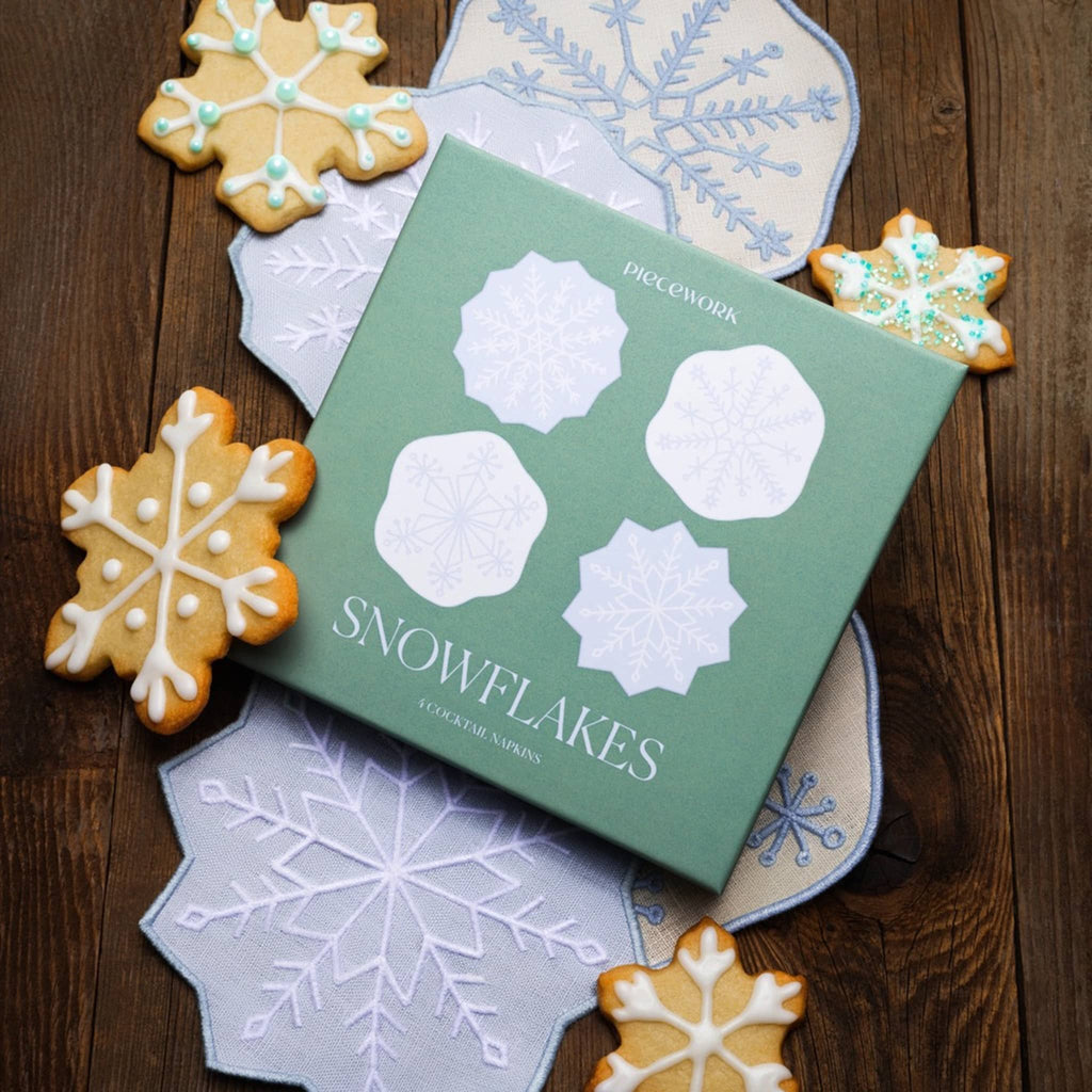 Snowflake linen napkins with green packaging box and snowflake cookies on a wooden surface.