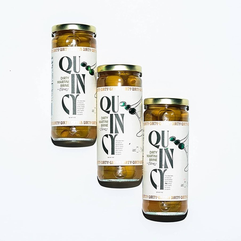 Quincy dirty martini brine and olives in jar, 3 are shown on a white background.