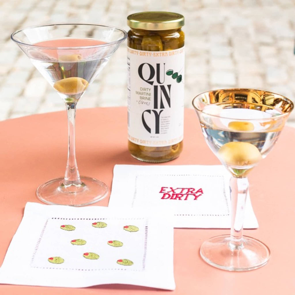 Quincy dirty martini brine and olives in jar, shown with 2 types of martini glasses and cloth napkins.