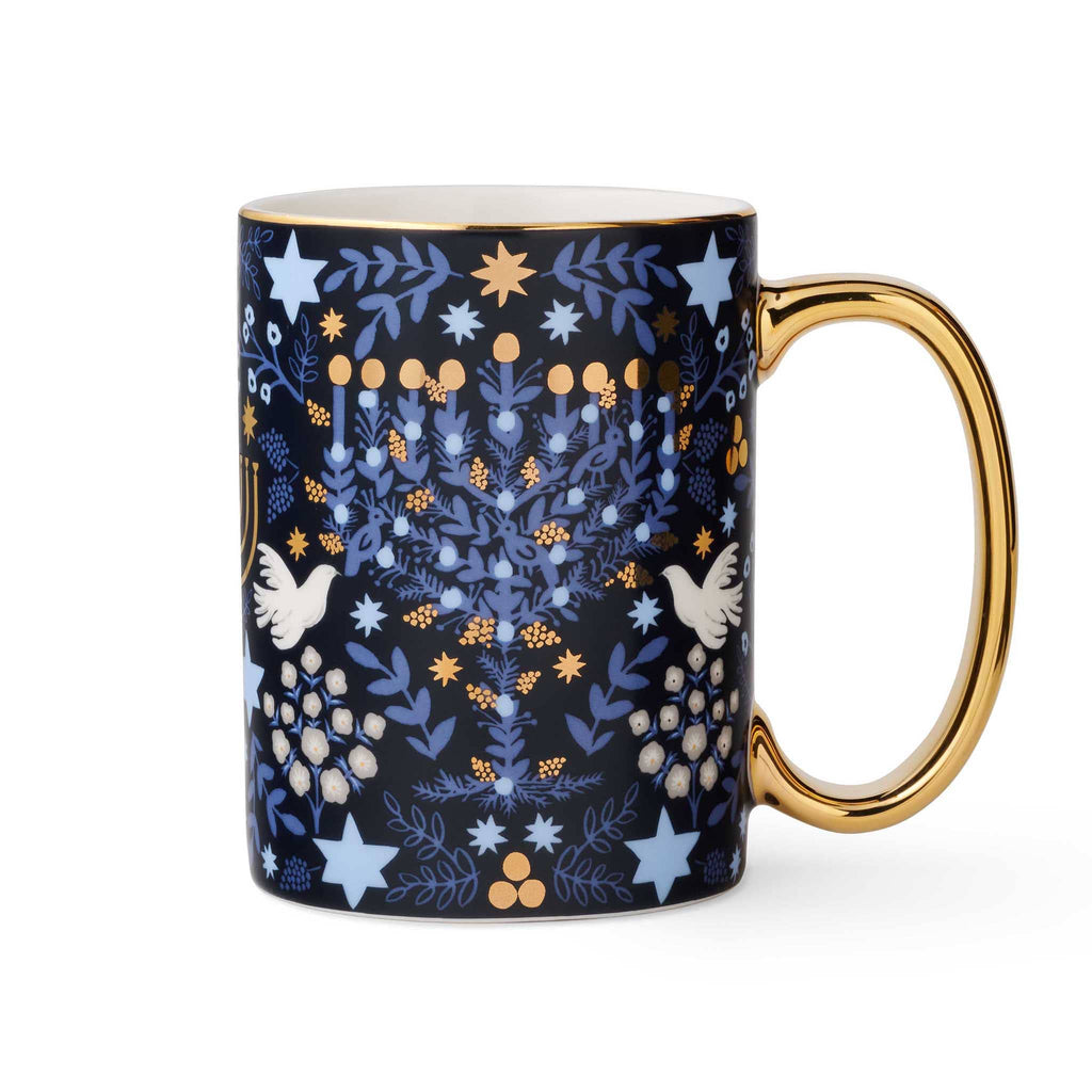 Mug with rifle paper laurel menorah pattern featuring stars, laurel, and birds on a navy background with gold rim and handle on the right, on a white background.
