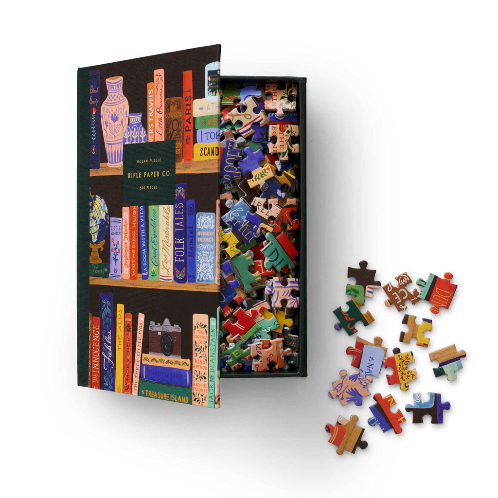 Rifle Paper Co. 500 Piece Bookshelf Jigsaw Puzzle in book box packaging, lid open showing pieces inside.