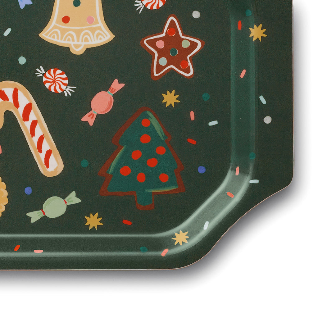 Rifle Paper Co. vintage-style bent ply rectangle holiday serving tray with illustrations of colorful cutout cookies with candy and sprinkles on a dark green background, detail of cutout corner.